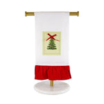 White hand towel with a Christmas tree patch and red ruffled hem hanging on a gold stand