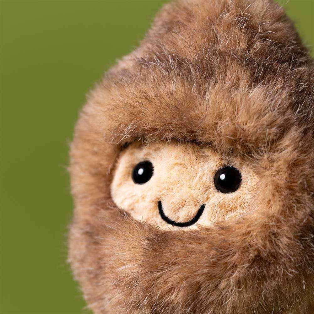 Close-up of a plush toy with a brown fuzzy exterior and beige face on a green background