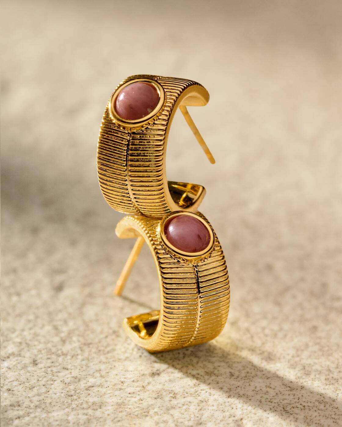 Gold hoop earrings with textured ribbed surface and round pink stone inlay