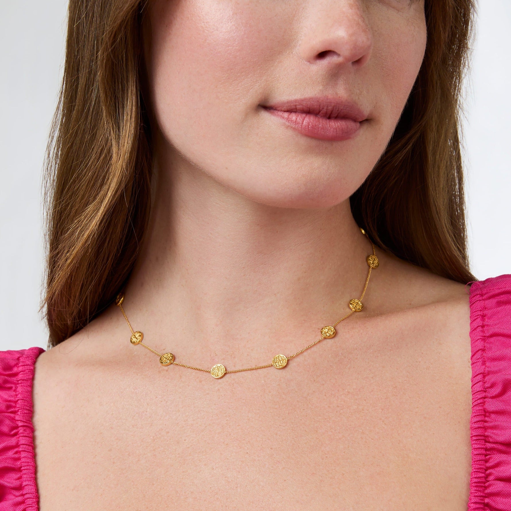 Gold chain necklace with small circular charms worn by a woman