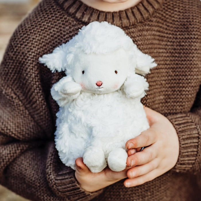 A small white plush lamb toy with embroidered features, being held by a child.