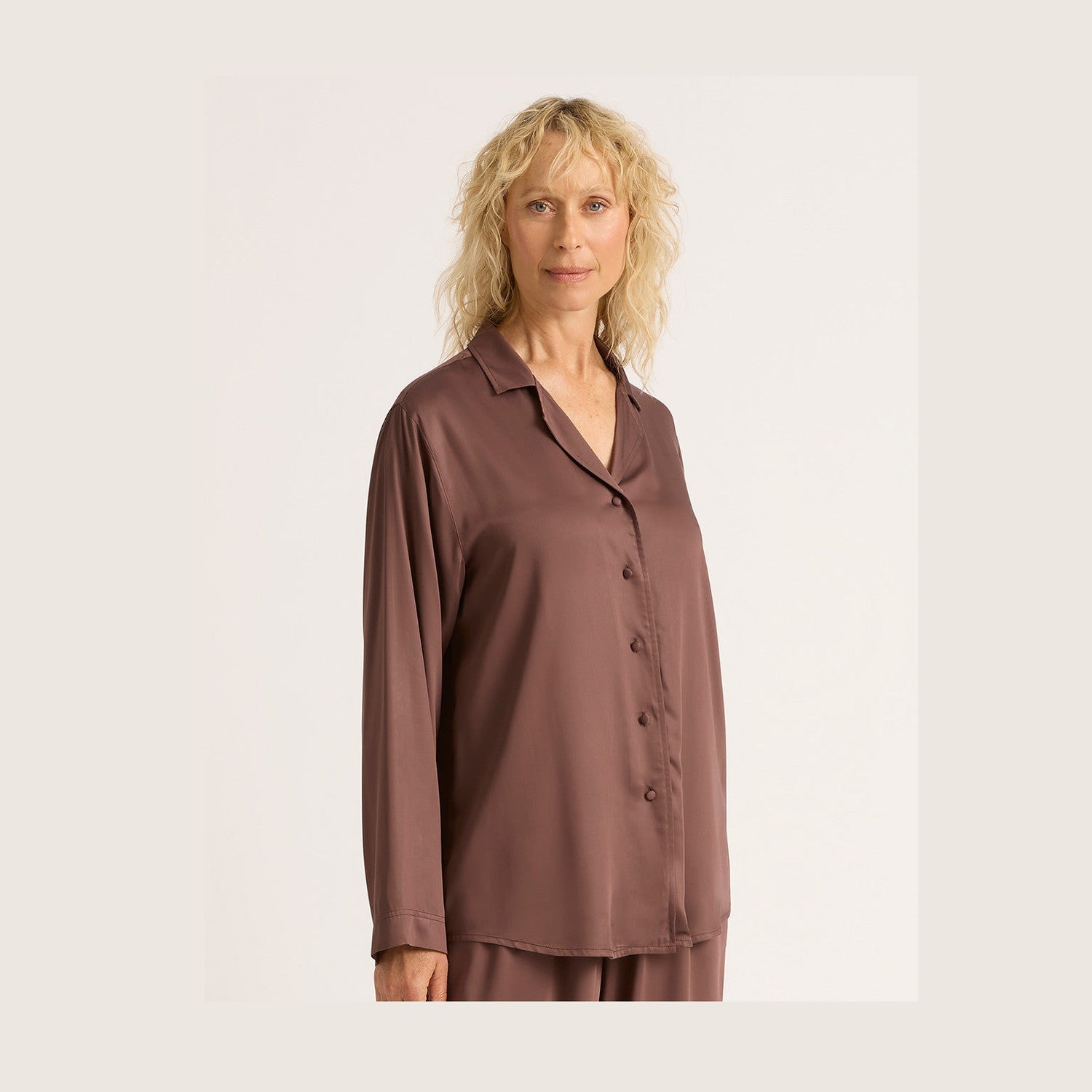 Woman wearing a brown satin pajama shirt on a plain background