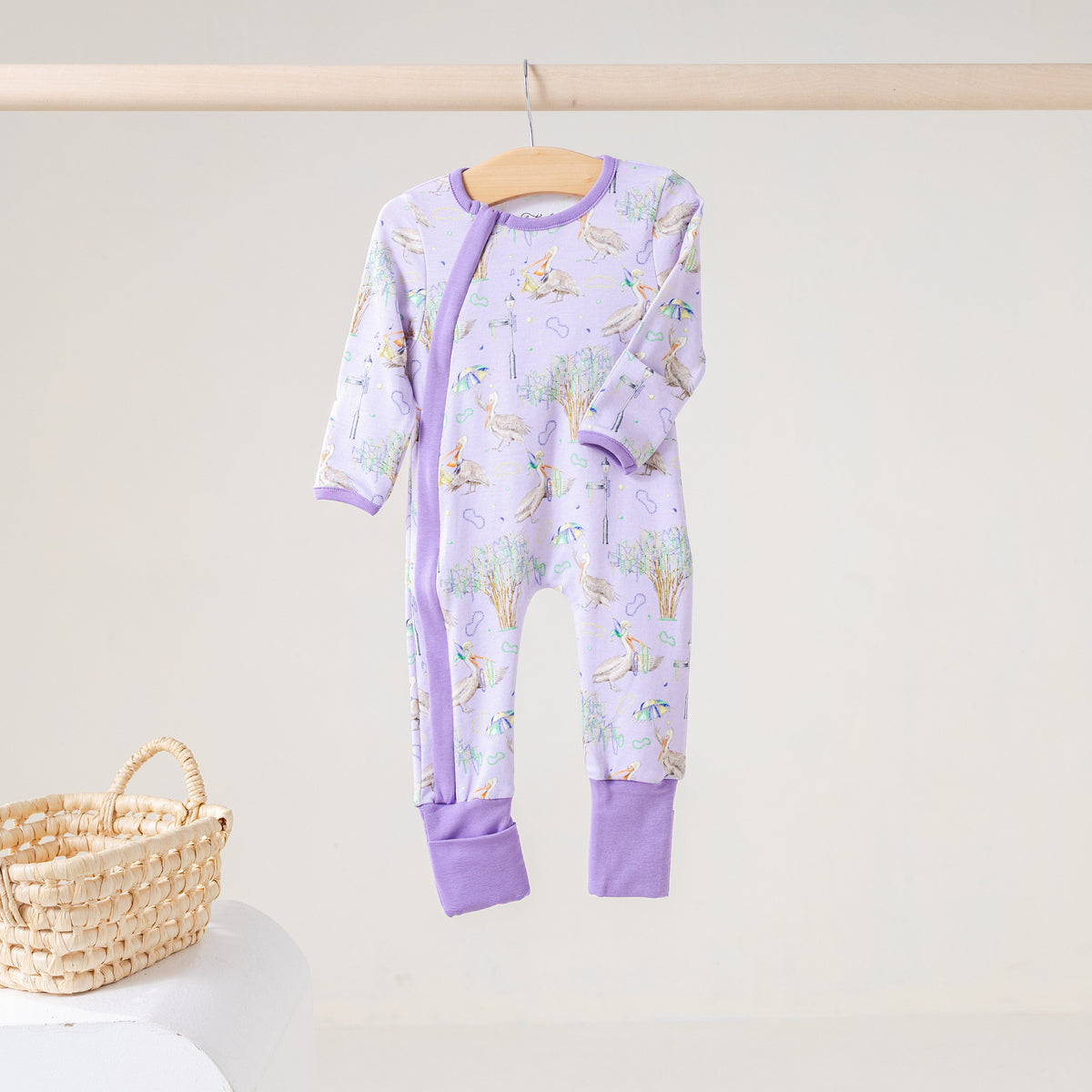 Lavender zip footie with a print of pelicans, oak trees, parasols and Mardi Gras beads