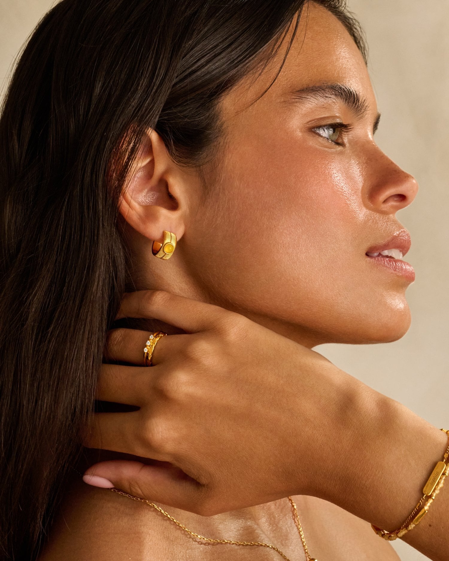 Woman wearing gold hoop earrings with amber stone and a gold ring with small diamonds