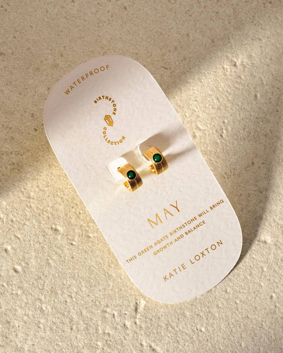 Gold hoop earrings with green agate stones on a May birthstone display card