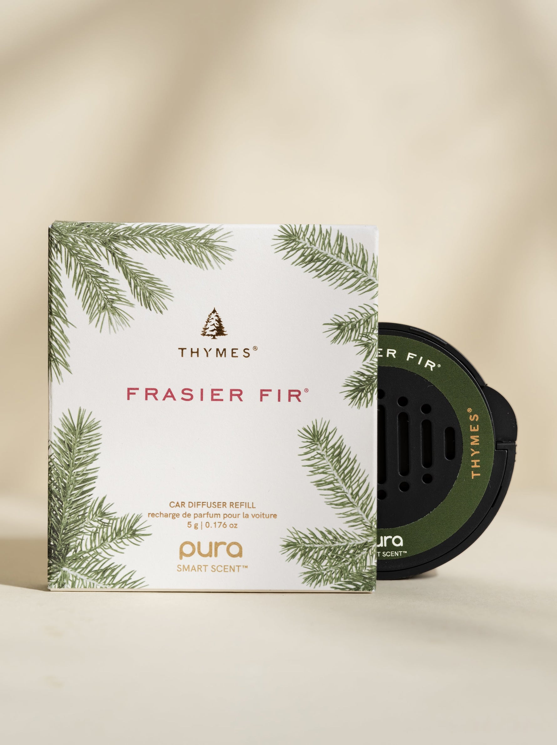 Studio photograph of Thymes Frasier Fir Pura Smart Scent car diffuser refill featuring the iconic brand tree logo, green fir needle illustrations, and a black circular scent pod on a neutral beige background