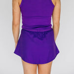 Person wearing a purple tank top and matching athletic skirt from behind