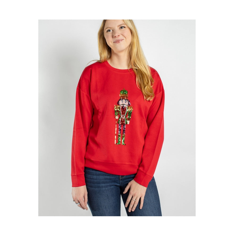 Woman wearing a red sweatshirt with a sequined nutcracker graphic