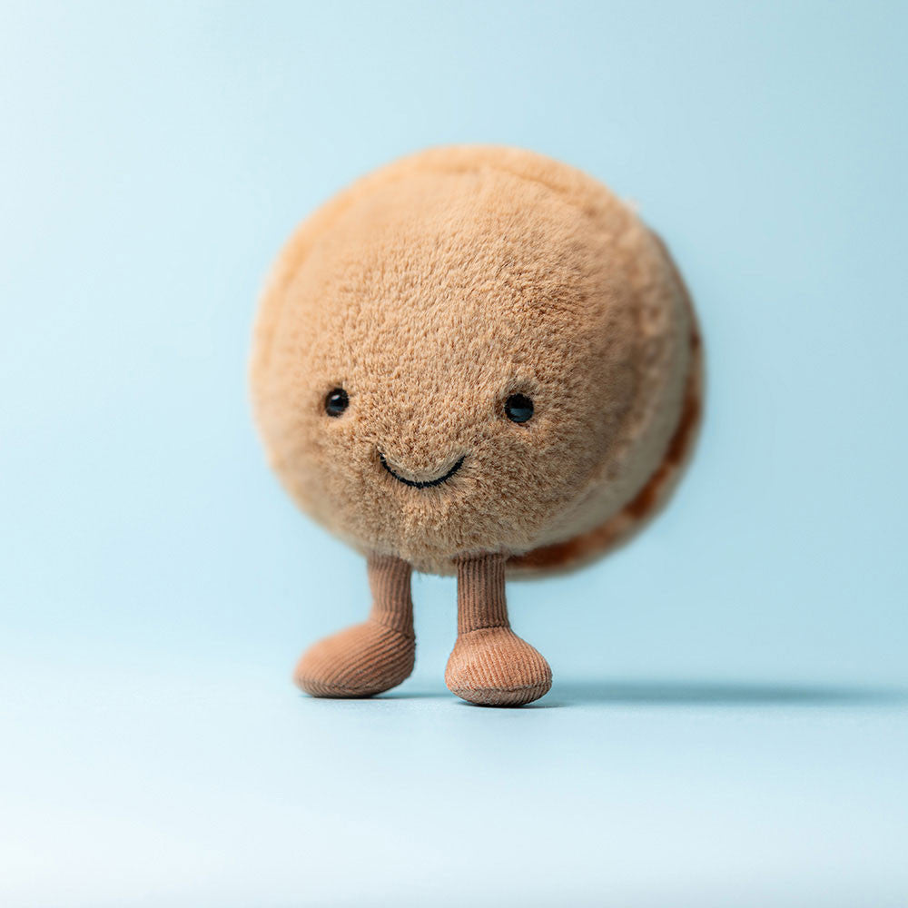 Tan plush macaron with a smiling face standing on corduroy legs against a light blue background