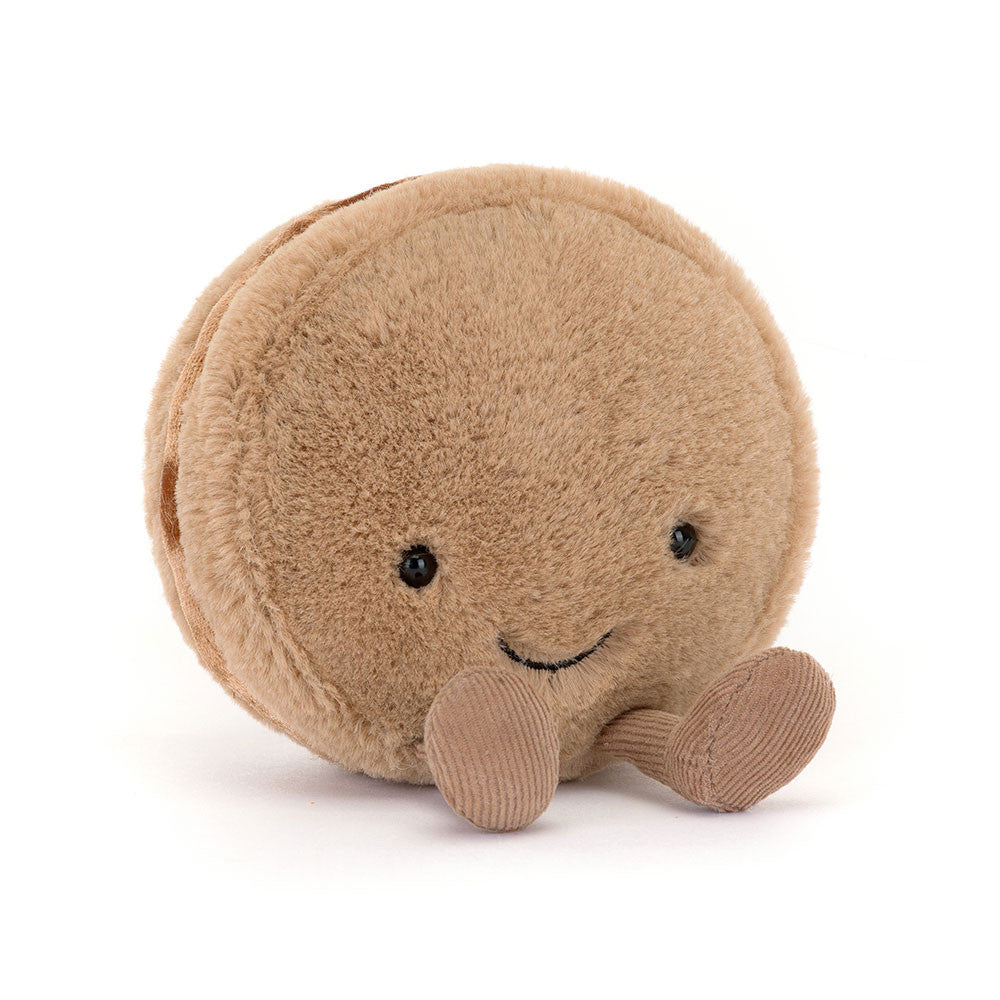 Tan plush macaron with a smiling face and brown corduroy feet, angled view
