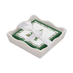 Stack of holiday napkins with holly print tied with a white ribbon in a white ceramic tray