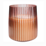 A large pink glass candle with a proprietary soy-blend wax, designed with vertical ridges and a warm light hue.