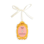 Oval gold framed tag with pink center reading Press For Champagne with a white ribbon tie