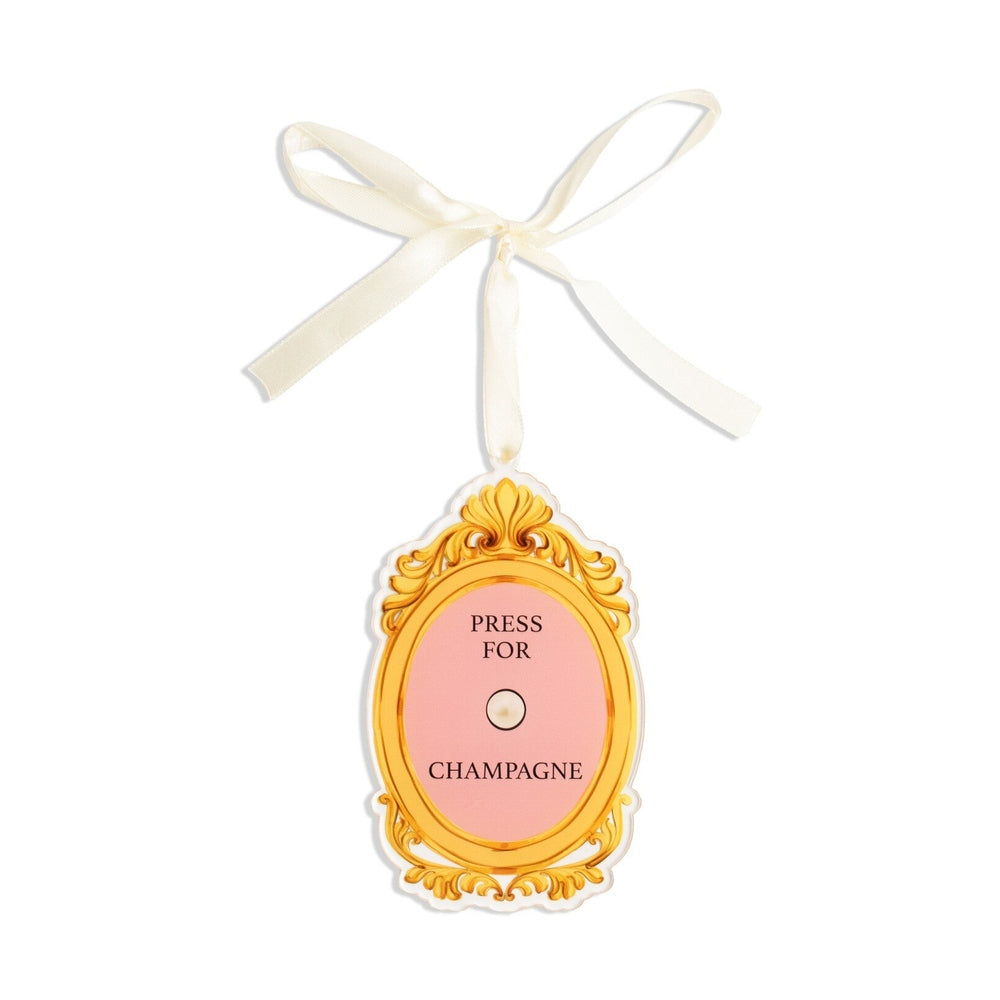 Oval gold framed tag with pink center reading Press For Champagne with a white ribbon tie