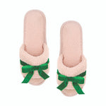 Pair of pink slippers with green bows on a white background