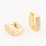 Gold-plated jewelry featuring a pair of rectangular huggie hoop earrings embellished with rows of pave-set shimmering clear stones against a minimalist white background