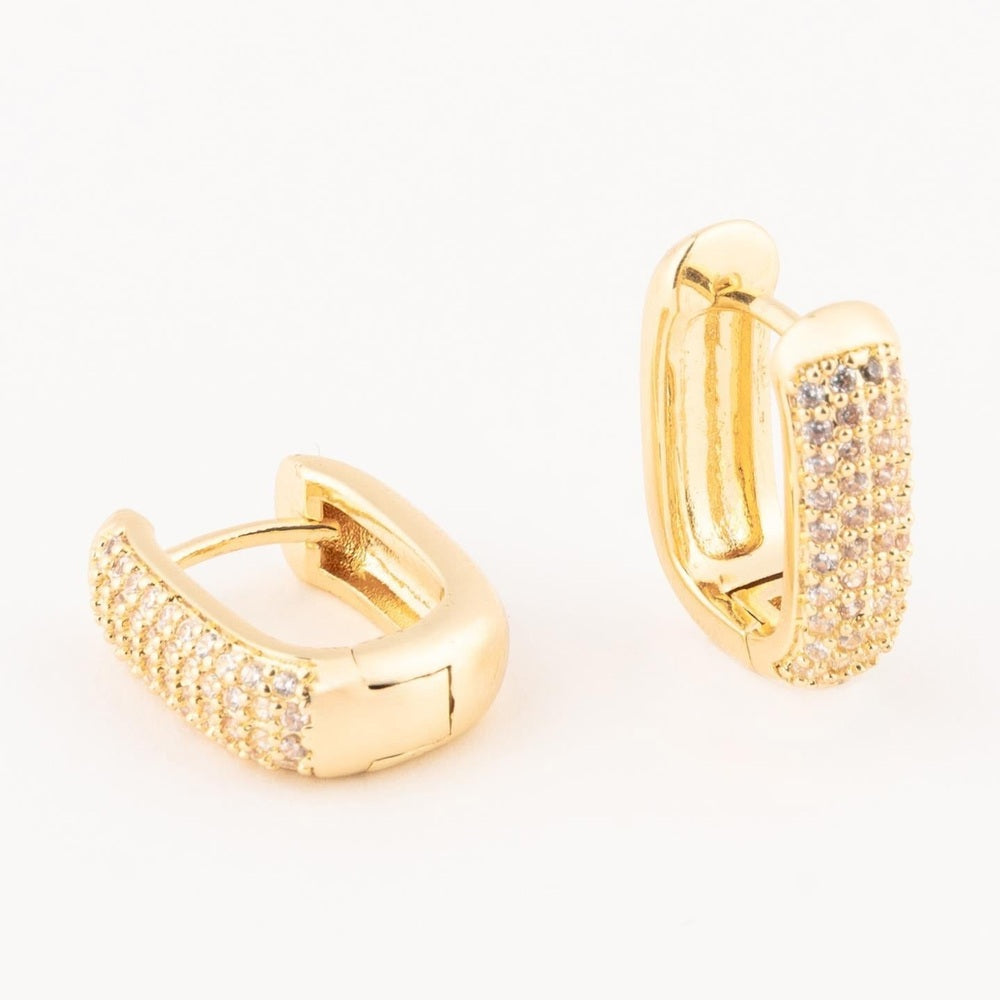 Gold-plated jewelry featuring a pair of rectangular huggie hoop earrings embellished with rows of pave-set shimmering clear stones against a minimalist white background