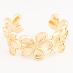 Polished gold-tone metal floral cuff bracelet on a white background featuring sculpted five-petal flowers with textured stippled centers and a satin-brushed finish on the petals