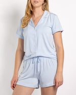 Woman wearing a light blue short sleeve button down pajama top and matching shorts with white piping