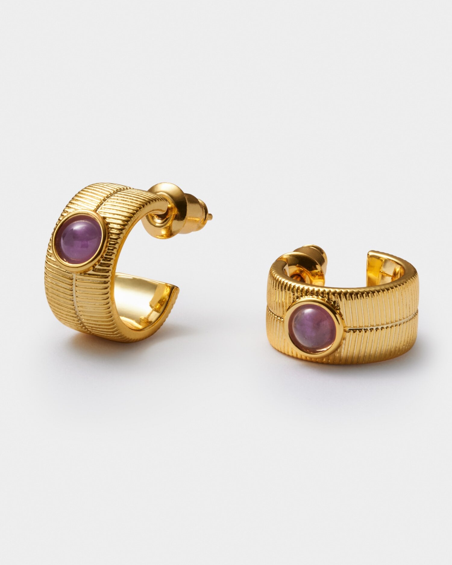 Gold hoop earrings with vertical ribbed texture and a central purple cabochon stone