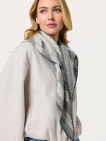 Woman in a cream coat wearing a gray striped triangle scarf