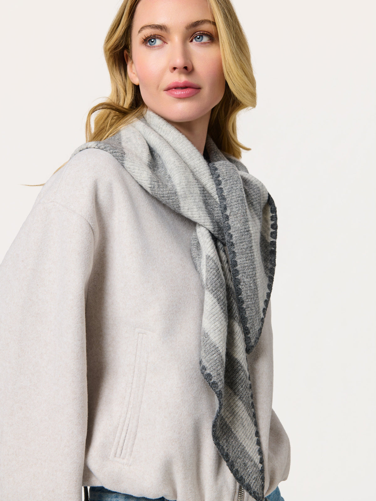 Woman in a cream coat wearing a gray striped triangle scarf