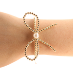 Gold beaded bracelet with a pearl on a wrist against a white background