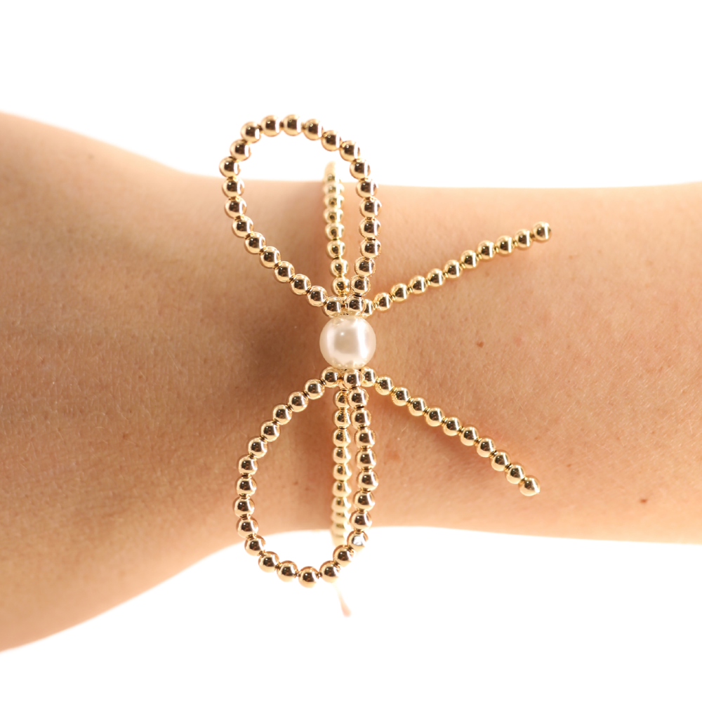 Gold beaded bracelet with a pearl on a wrist against a white background