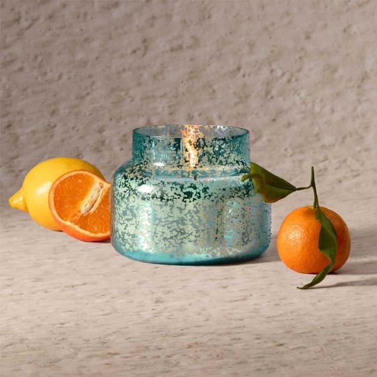 Blue mercury glass candle holder with a lit candle, surrounded by fruits on a wooden surface.