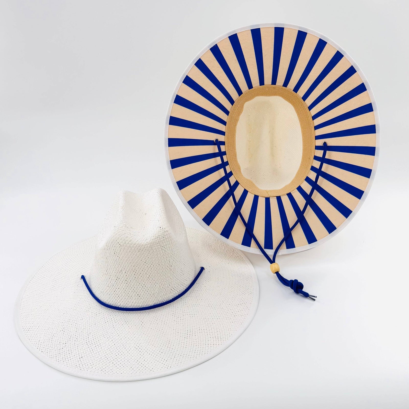 Two sunhats, one white with blue band and the other beige with blue and beige striped design, on a light gray background.