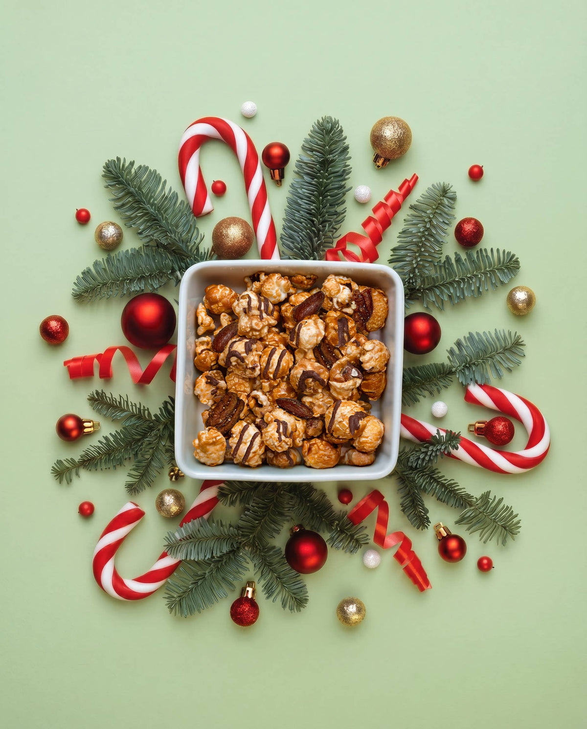 Bowl of chocolate-drizzled caramel popcorn surrounded by pine, candy canes and red ornaments
