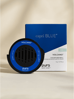 Product photograph by Capri Blue and Pura of a Volcano car diffuser refill and its cobalt blue packaging box featuring a circular black device with a bright blue rim and small air vents set against a minimalist neutral background