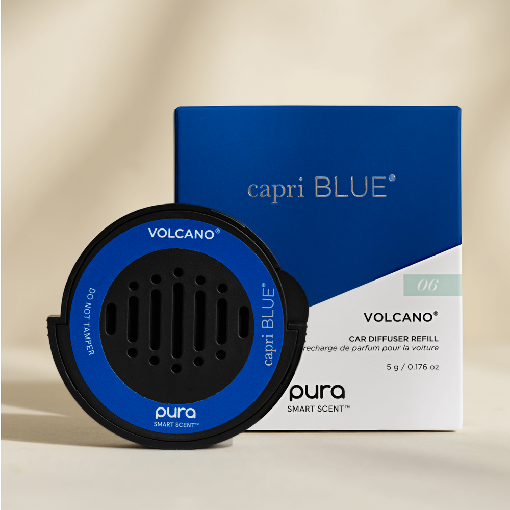 Product photograph by Capri Blue and Pura of a Volcano car diffuser refill and its cobalt blue packaging box featuring a circular black device with a bright blue rim and small air vents set against a minimalist neutral background