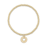 Gold beaded stretch bracelet with a round charm featuring a cutout heart