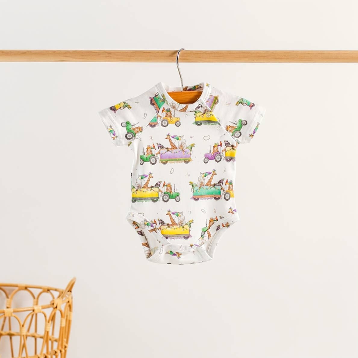 White short-sleeve baby bodysuit with a print of giraffes and zoo animals riding colorful parade floats