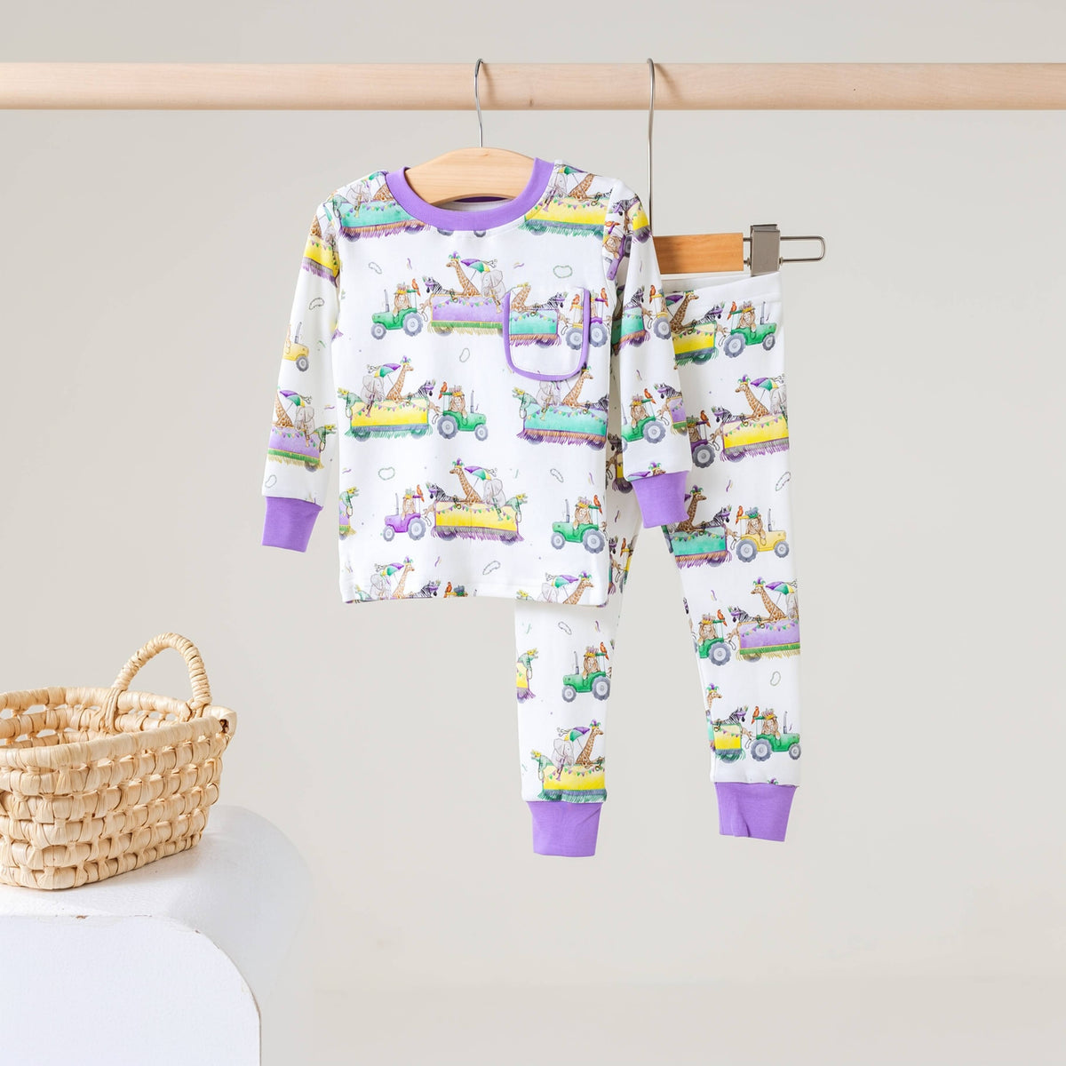 White two-piece pajama set with lavender cuffs and a print of zoo animals riding colorful parade floats
