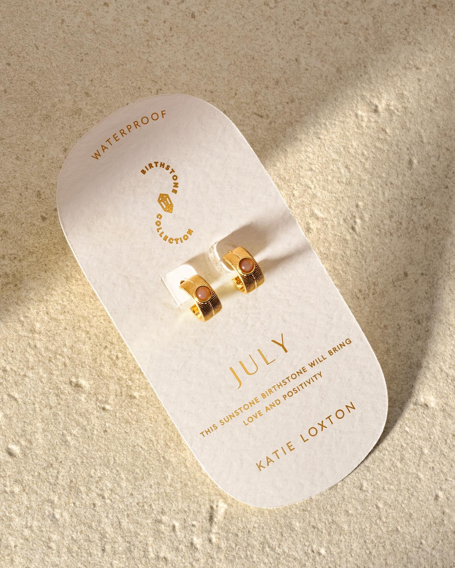 Gold hoop earrings with sunstone gems on a July birthstone collection display card