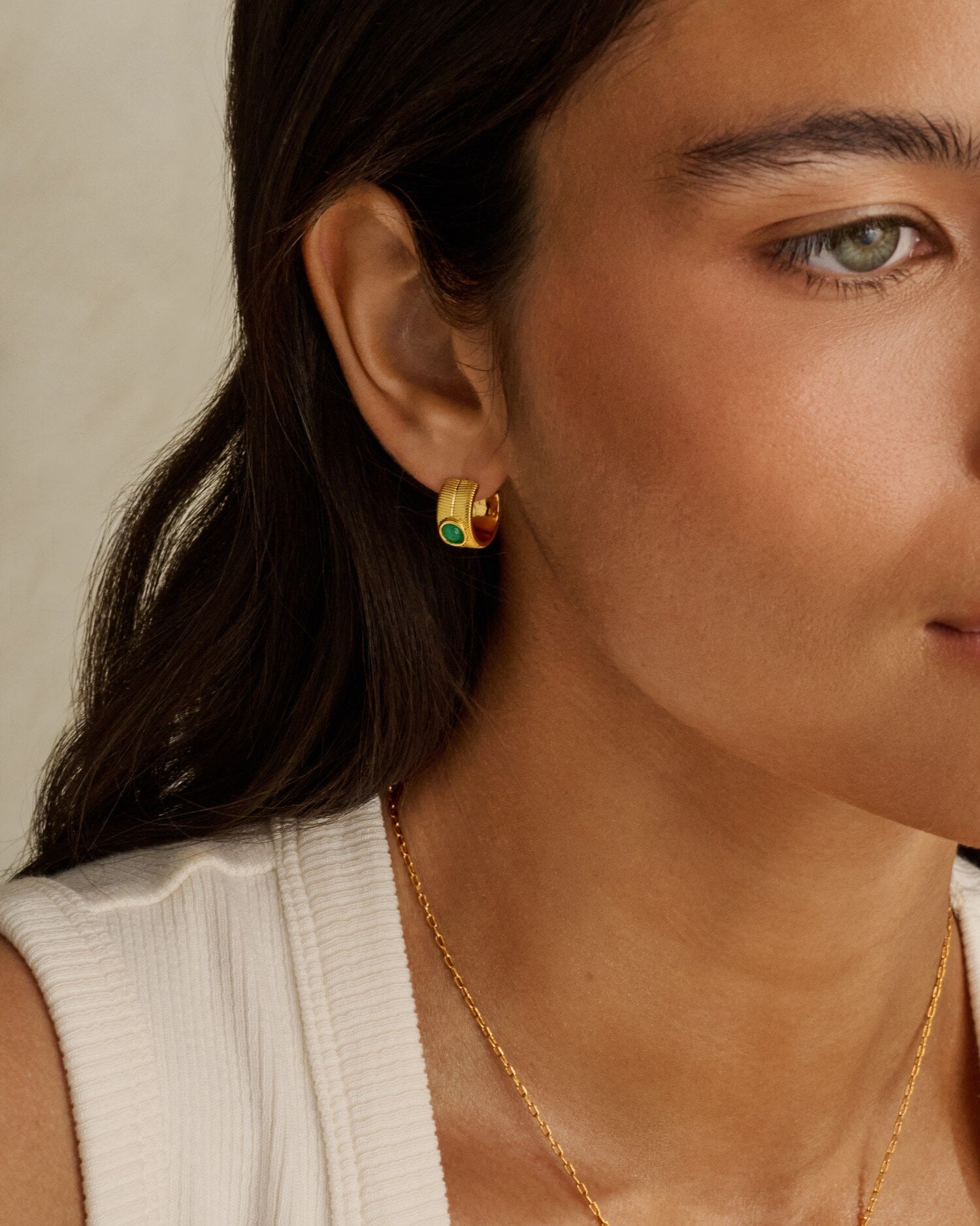 Gold hoop earring with a small green stone worn on a person ear