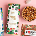 Poppy Reindeer Crunch popcorn tin in a geometric holiday print beside a bowl of caramel popcorn