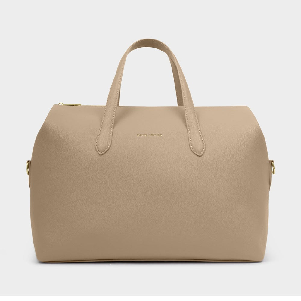 Product photograph by Katie Loxton of a taupe vegan leather weekend bag on a plain grey background featuring a gold-stamped brand logo and matching top handles with metallic hardware accents