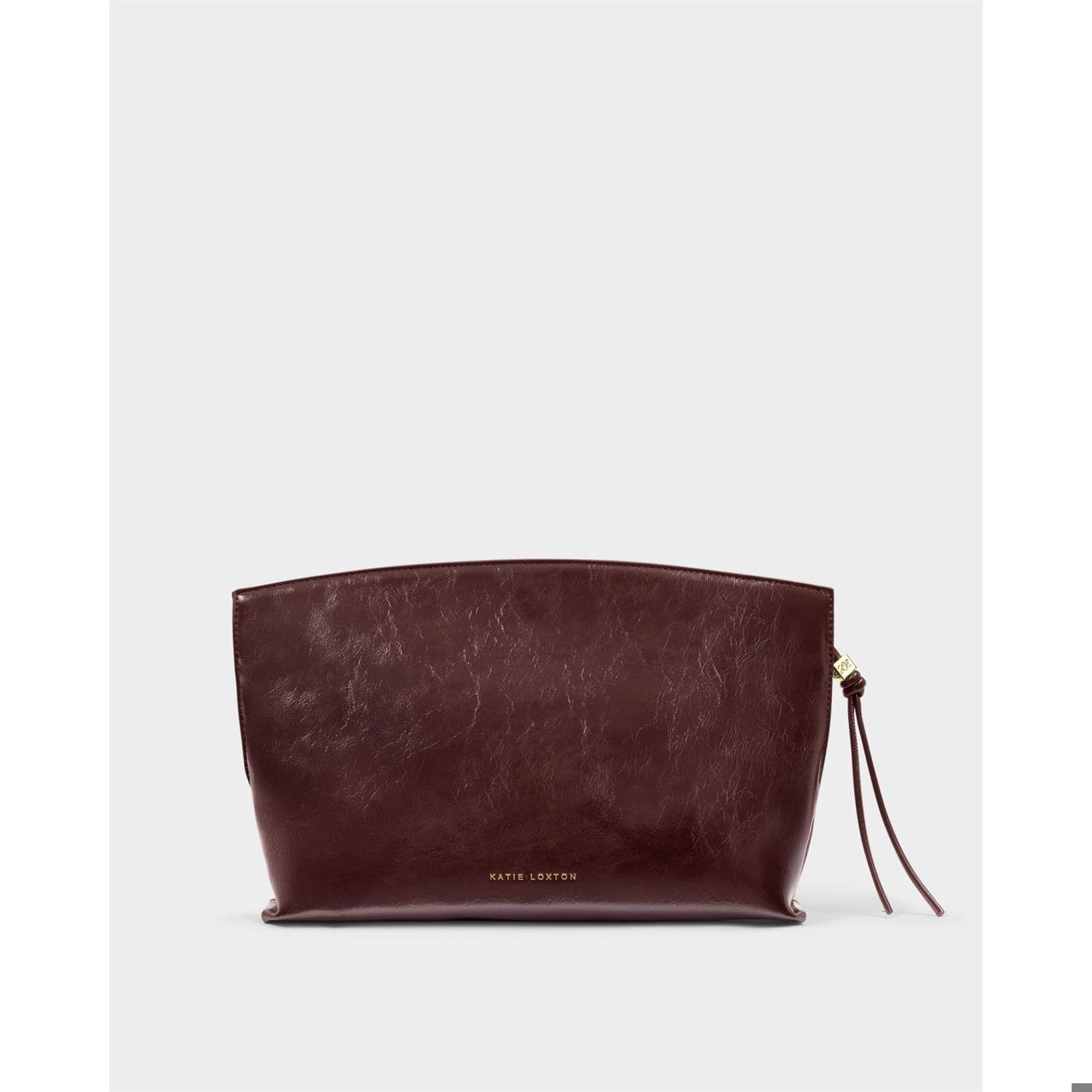 Vegan leather clutch bag by Katie Loxton showcasing a dark burgundy crinkled texture, gold-tone embossed logo, and a knotted zip pull set against a neutral studio backdrop
