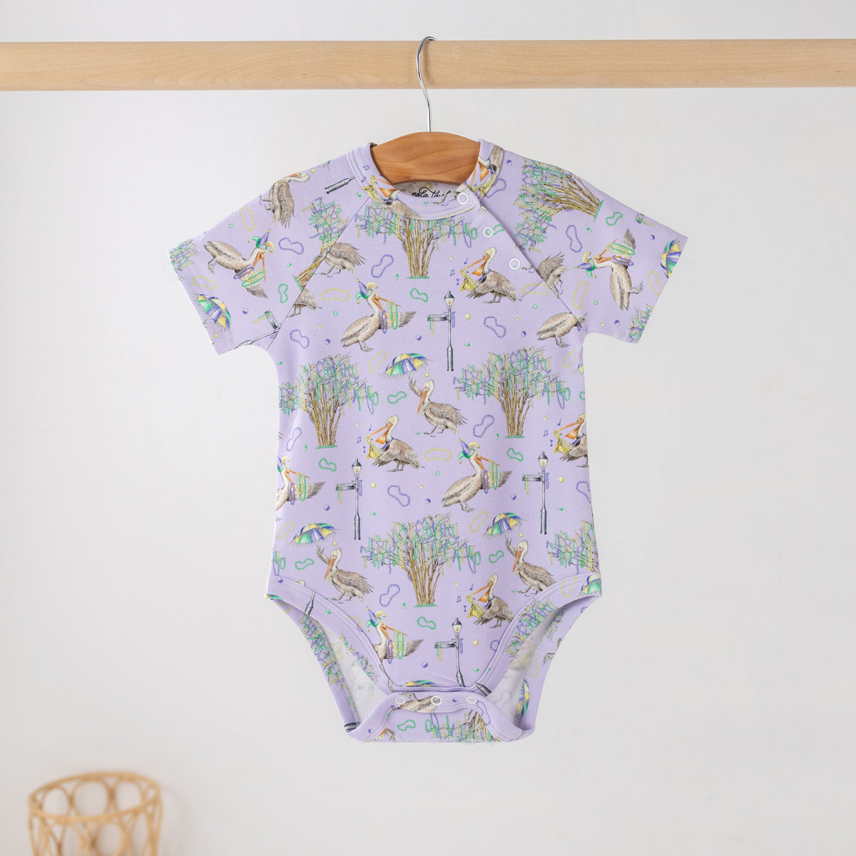 Lavender short-sleeve baby bodysuit with a print of pelicans, oak trees, parasols and Mardi Gras beads