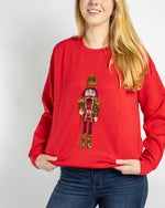 Woman wearing a red sweatshirt with a sequined nutcracker graphic