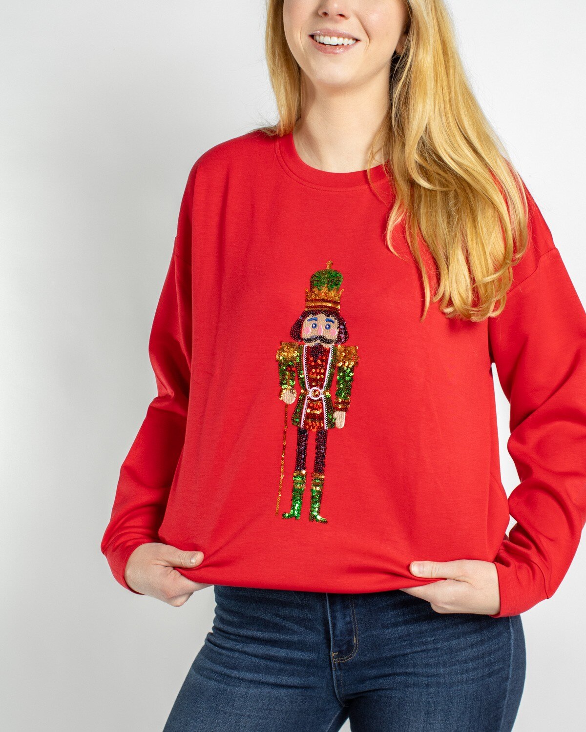 Woman wearing a red sweatshirt with a sequined nutcracker graphic