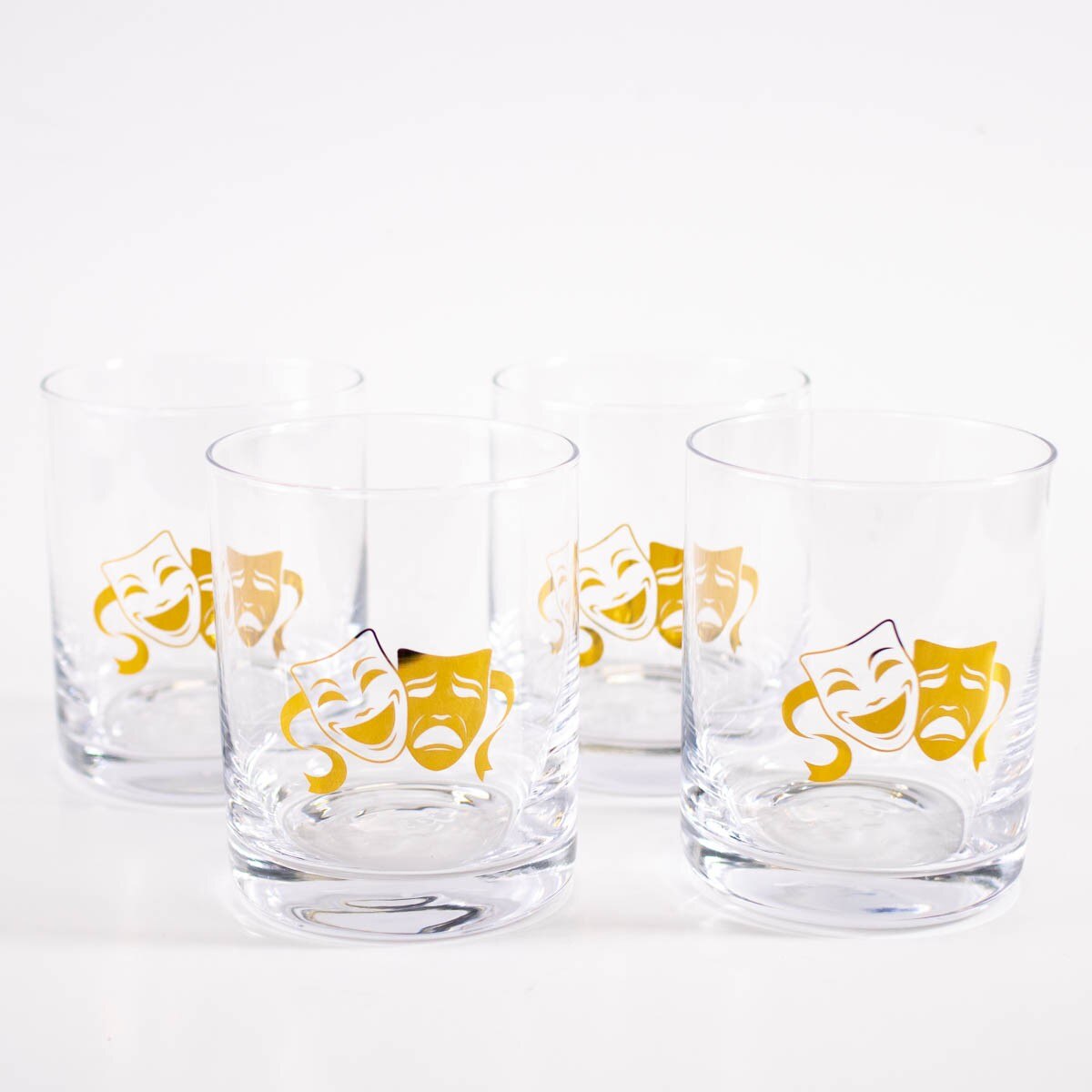 Four clear glass tumblers with gold comedy and tragedy mask icons