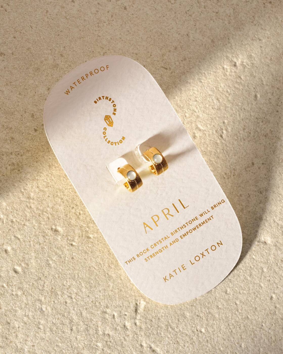 Gold hoop earrings with rock crystal stones on a Katie Loxton April birthstone display card