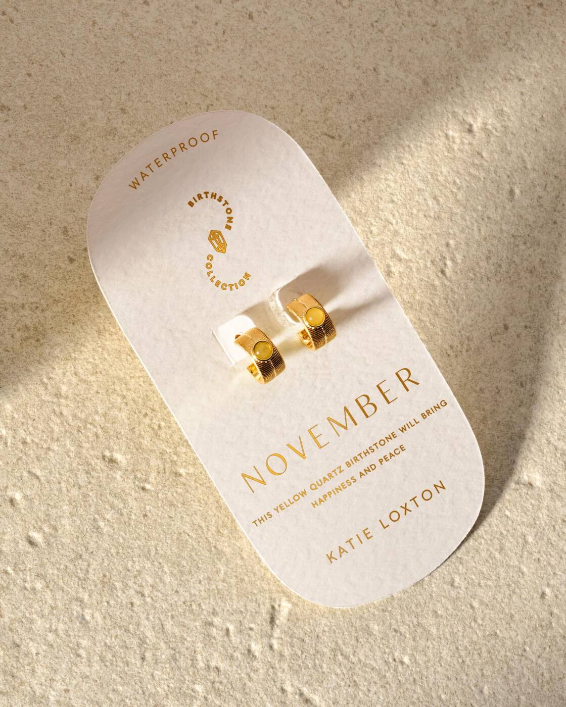 Gold hoop earrings with yellow quartz stones on a November birthstone display card