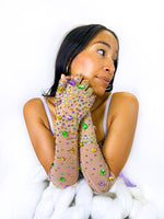Woman resting her chin on her hands wearing sheer long gloves covered in purple, green and gold gems