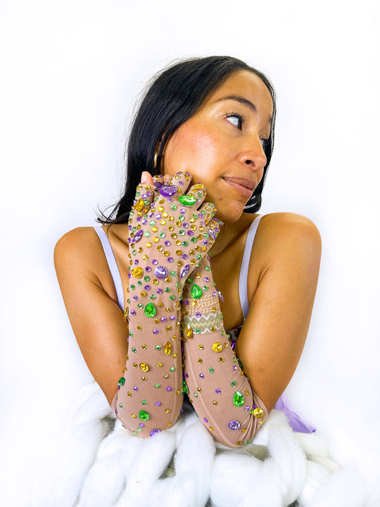Woman resting her chin on her hands wearing sheer long gloves covered in purple, green and gold gems