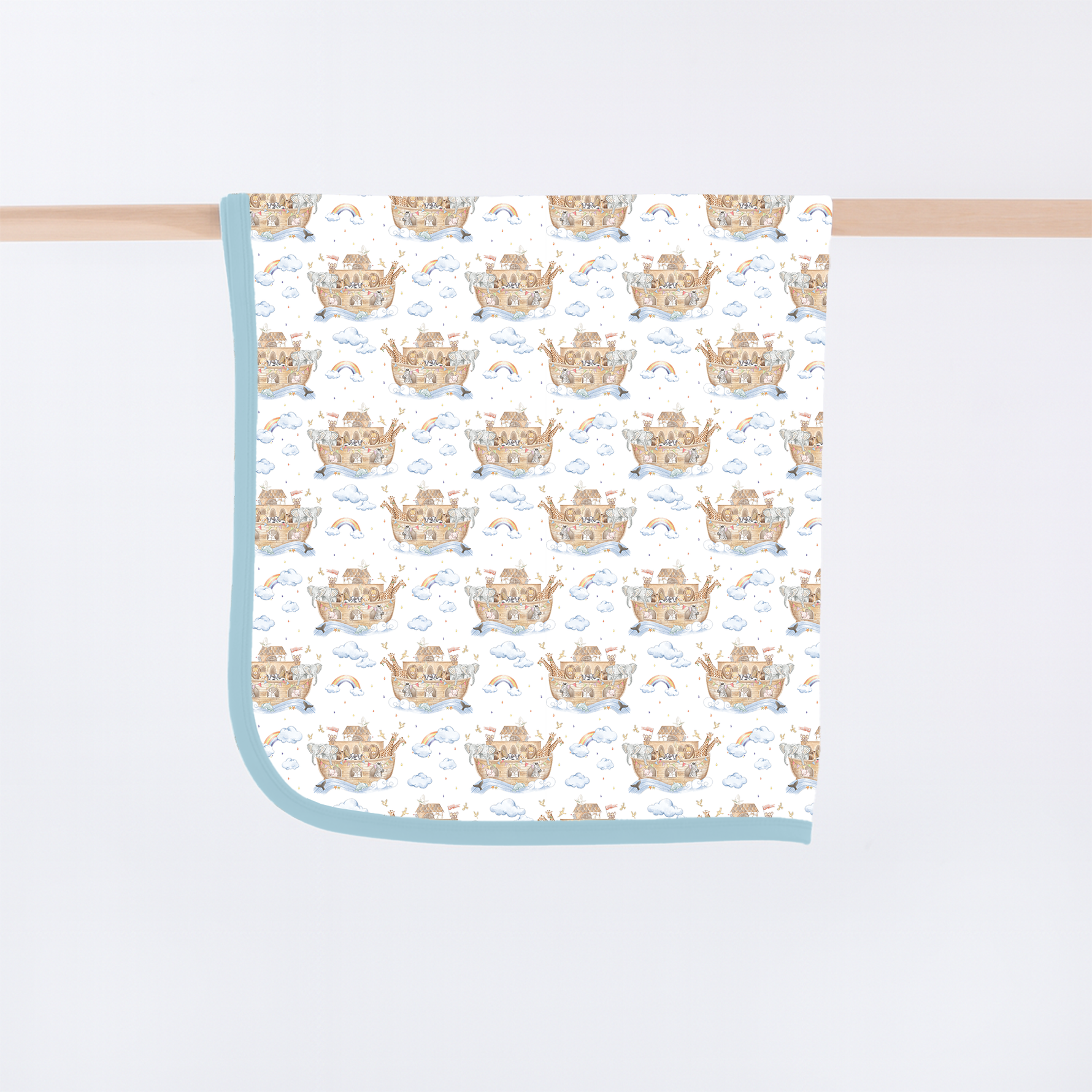 Watercolor illustration on a baby blanket featuring a repeat pattern of Noah's Ark sailing on blue waves with pairs of giraffes and elephants under pastel rainbows and fluffy white clouds with a light blue border